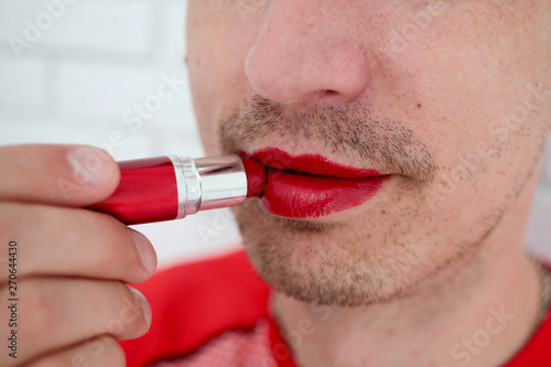 Close up of bearded man applying colorful red balm lipstick on his lips , on camera, lips, side view .