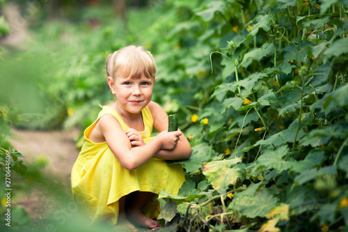 The girl in a yellow dress sits in a kitchen garden and holds a cucumber in hand