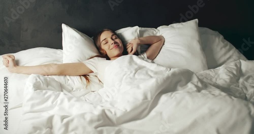 Beautiful awakening woman stretching in wide white bed, sunny fresh morning concept