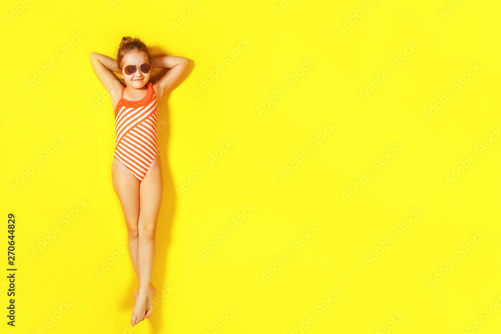Top view on the lying little girl with glasses. A child in a bathing suit resting on a yellow background. Summer concept.