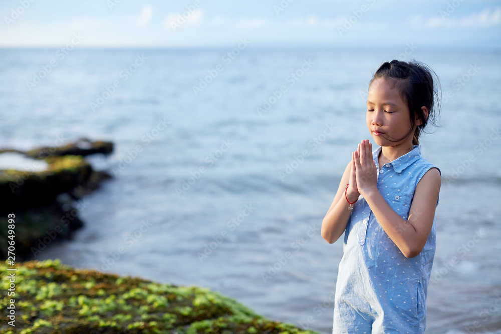 Cute beautiful asian little girl praying with hands closed at the seaside Cute beautiful asian little girl praying with hands closed at the seaside