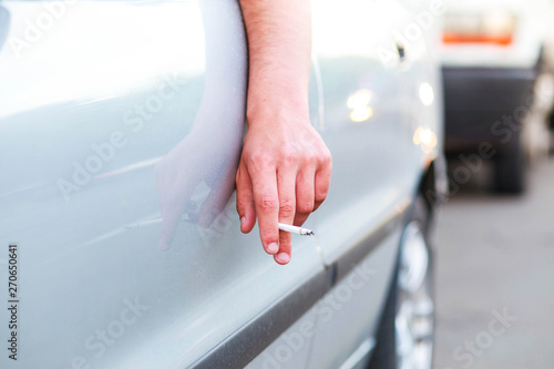 A man's hand is holding a cigarette butt through a car window. The theme of the unauthorized person throwing cigarette butts out onto the street.