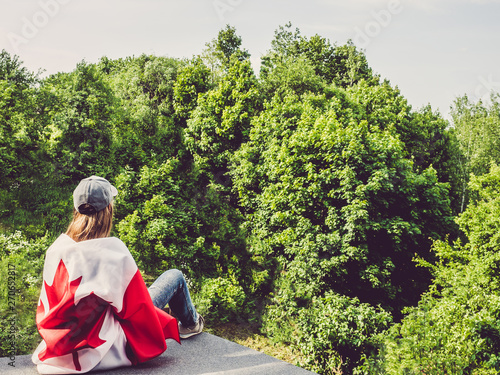 Cute woman and Canadian Flag on a background of trees and blue sky. View from the back, close-up. National holiday concept photo