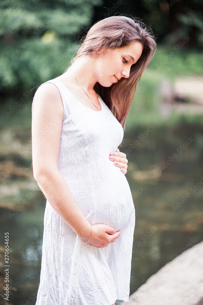 Beautiful pregnant woman walks in the park along the river Beautiful pregnant woman walks in the park along the river