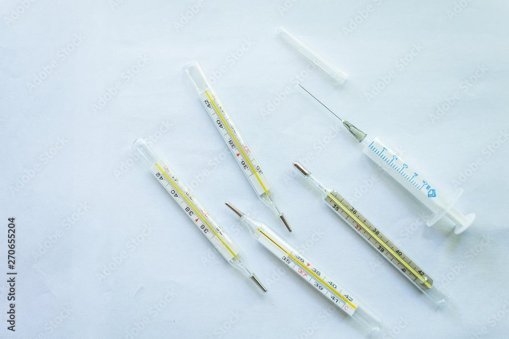 Four mercury thermometers and a disposable medical syringe on a white background Four mercury thermometers and a disposable medical syringe on a white background