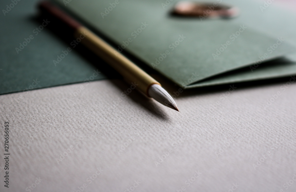 Close up of green coloured fine art paper, a green envelope with a golden seal and a wooden calligraphy brush laying on top of it Close up of green coloured fine art paper, a green envelope with a golden seal and a wooden calligraphy brush laying on top of it