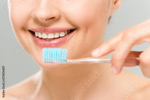 selective focus of woman smiling and holding toothbrush isolated on grey