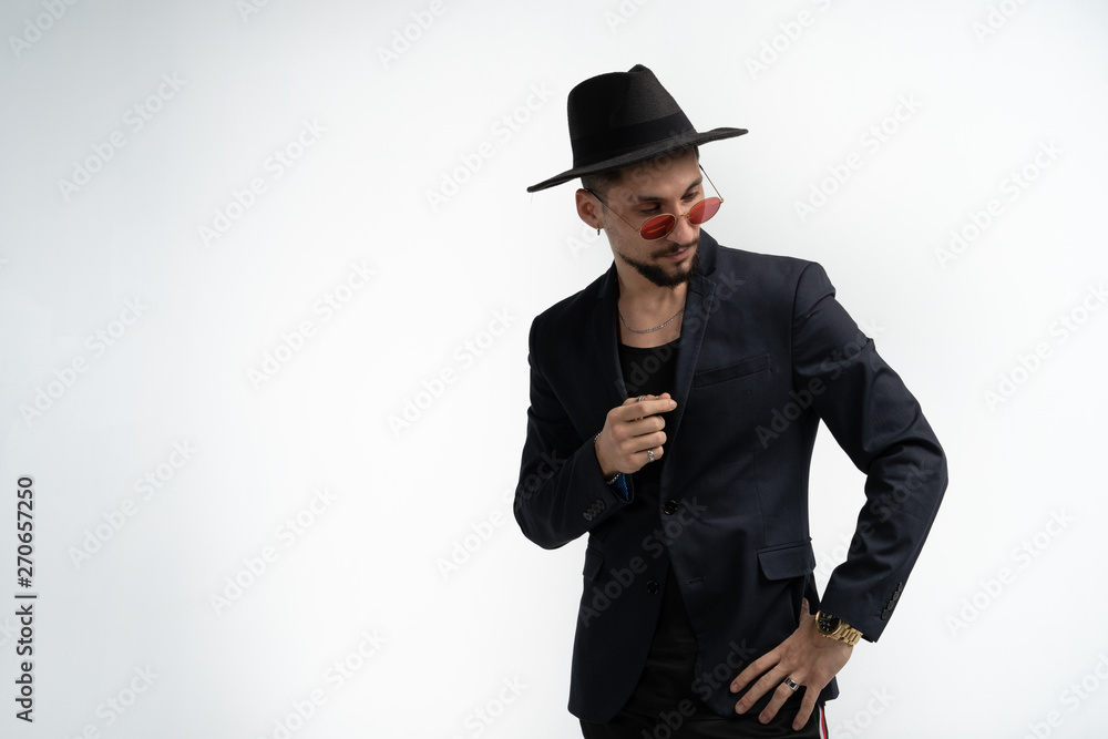 Handsome serious bearded man in black suit and hat, in red sunglasses posing isolated against white background, looking away Handsome serious bearded man in black suit and hat, in red sunglasses posing isolated against white background, looking away