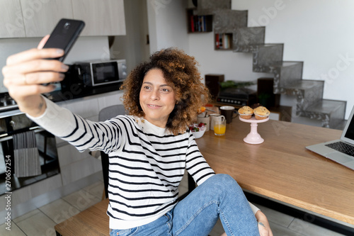 Woman sitting at home, taking smartphone selfie photo