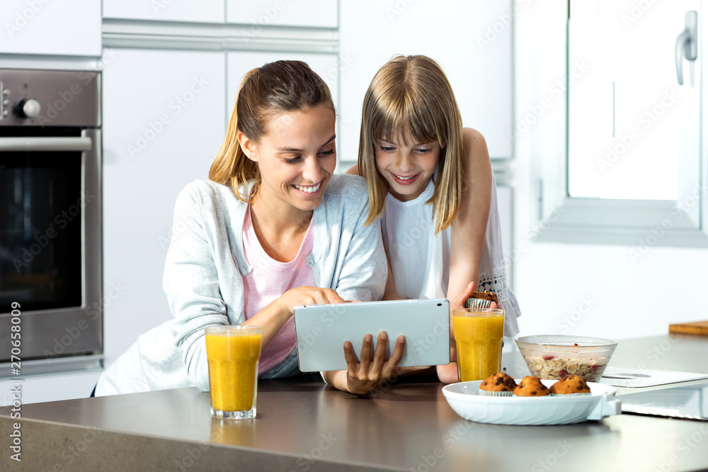 Pretty young mother and her daughter using digital tablet while having breakfast at home. Pretty young mother and her daughter using digital tablet while having breakfast at home.