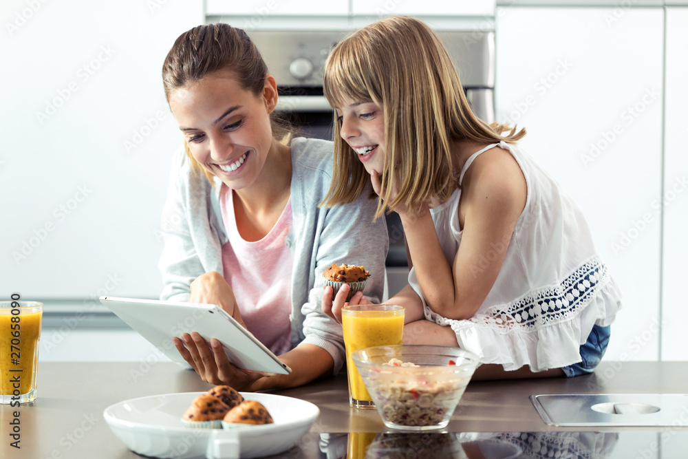 Pretty young mother and her daughter using digital tablet while having breakfast at home. Pretty young mother and her daughter using digital tablet while having breakfast at home.