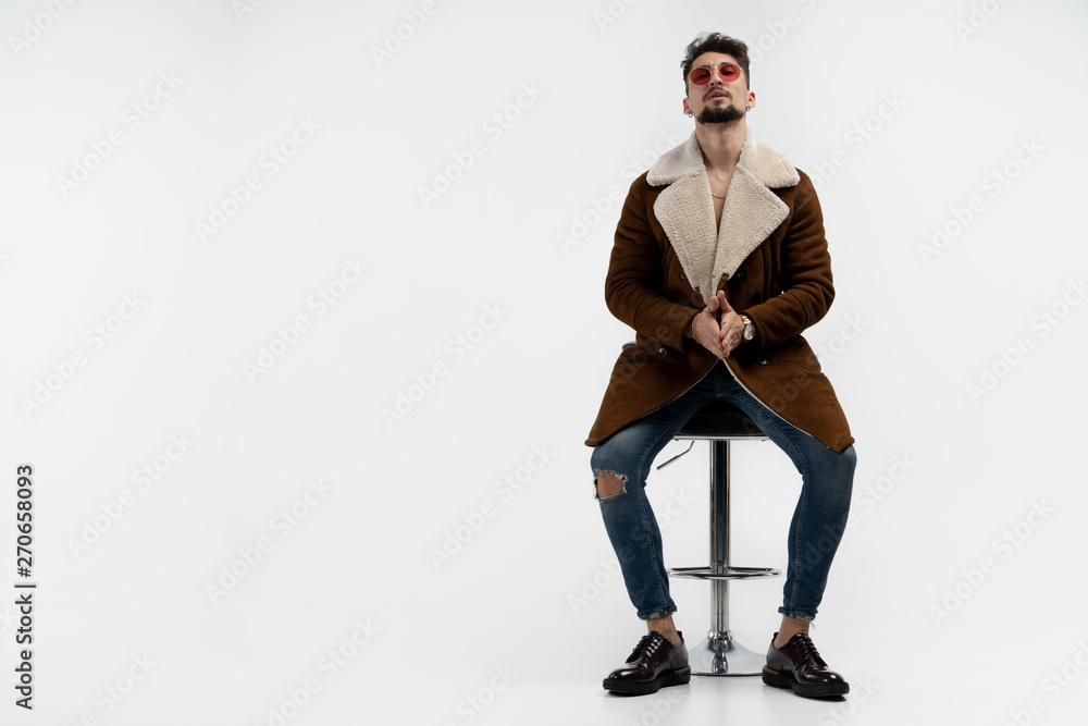 Serious bearded man in casual stylish clothes and red sunglasses sitting on bar stool, looking at the camera isolated over white background Serious bearded man in casual stylish clothes and red sunglasses sitting on bar stool, looking at the camera isolated over white background
