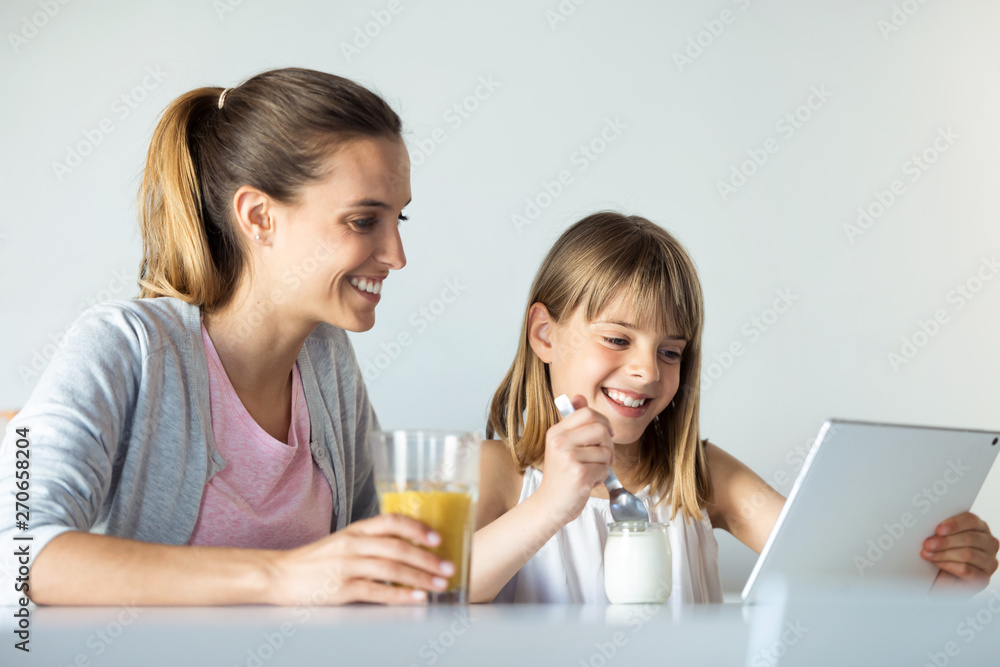 Pretty young mother and her daughter using digital tablet while having breakfast at home. Pretty young mother and her daughter using digital tablet while having breakfast at home.