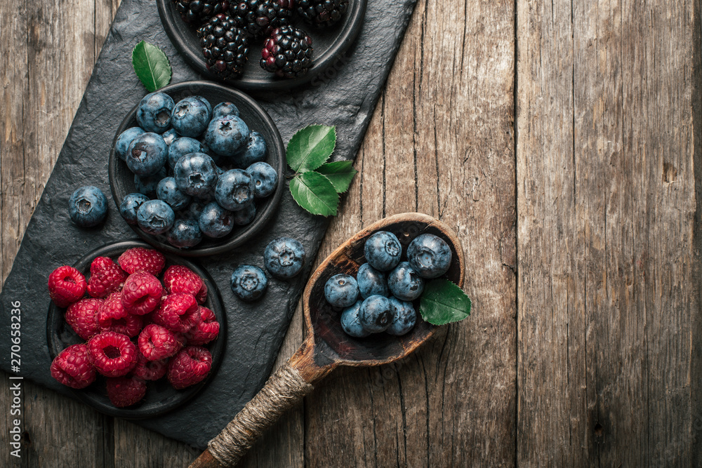 Fresh berries with raspberries, blueberries, blackberries in bowl on a stone stand on wood background.