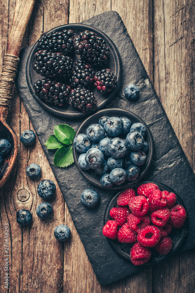 Fresh berries with raspberries, blueberries, blackberries in bowl on a stone stand on wood background. Fresh berries with raspberries, blueberries, blackberries in bowl on a stone stand on wood background.