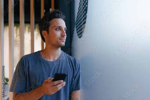 Young man with cell phone looking out of window photo
