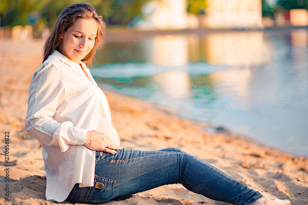 Beautiful pregnant woman sitting by the river at sunset Beautiful pregnant woman sitting by the river at sunset