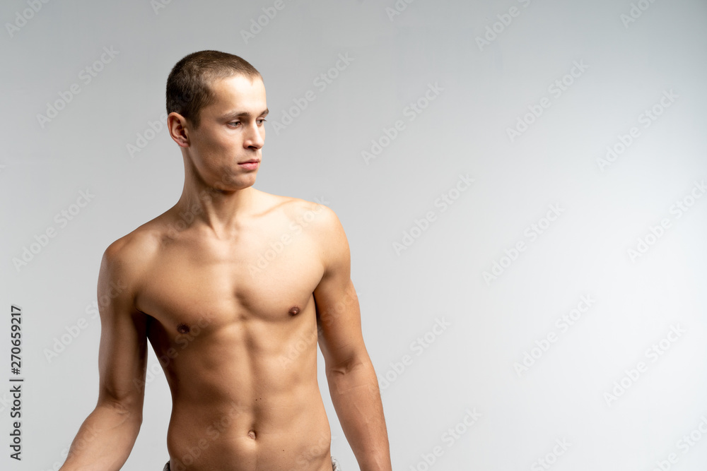 Serious muscular young man with naked torso, looking down, isolated over grey background, copyspace for your text