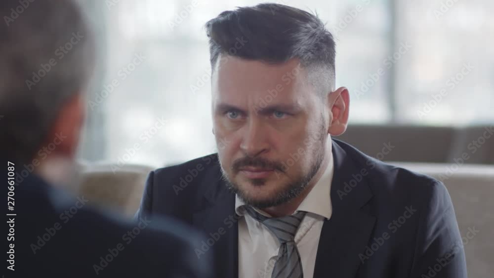 Back view of Caucasian businessman sitting on couch, listening to boss sitting in front of him and loosen his tie Back view of Caucasian businessman sitting on couch, listening to boss sitting in front of him and loosen his tie