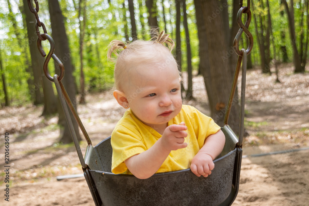 adorable blond caucasian toddler in the swing at the playground adorable blond caucasian toddler in the swing at the playground
