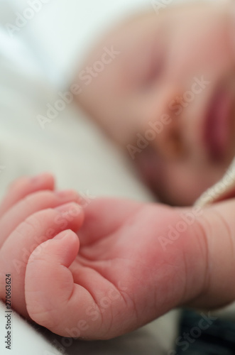 Hands of sleeping newborn baby. Face in shallow depth of field.