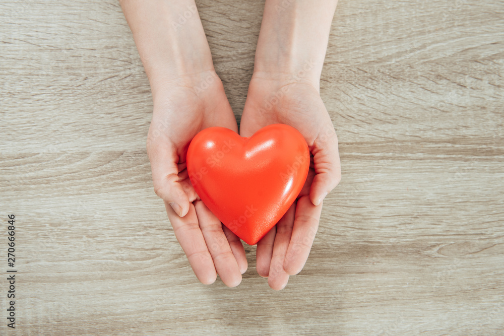 partial view of woman holding plastic heart on wooden surface partial view of woman holding plastic heart on wooden surface