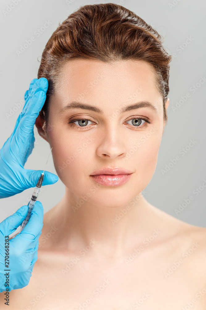 cropped view of cosmetologist holding syringe near face of beautiful and naked woman isolated on grey