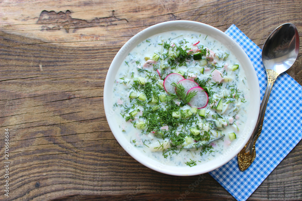 Okroshka is a traditional Russian summer cold soup in a ceramic bowl. Ingredients potatoes, radishes, cucumbers, dill, eggs, kefir (yogurt), sausage. Summer yogurt cold soup on a wooden table. Selecti Okroshka is a traditional Russian summer cold soup in a ceramic bowl. Ingredients potatoes, radishes, cucumbers, dill, eggs, kefir (yogurt), sausage. Summer yogurt cold soup on a wooden table. Selecti