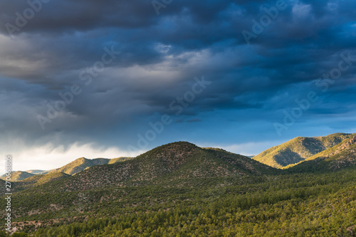 Sunset illuminates the pine forest clad hills under a dramatic sky of dark clouds - the Sangre de Cristo Mountains near Santa Fe, New Mexico