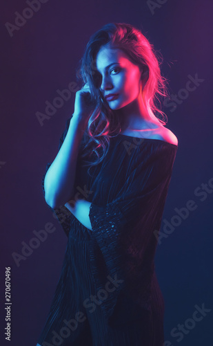 Beautiful ,young blonde with bright scarlet lips and expressive eyes in a black jumpsuit in neon light blue and red lamps.