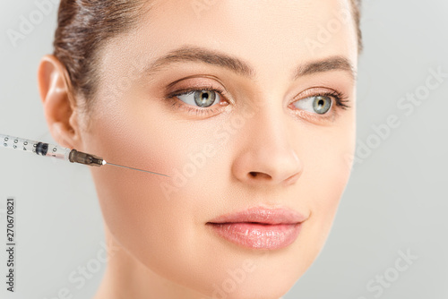 close up of syringe near face of attractive woman isolated on grey