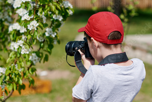 Schoolboy is taking picture of blossoming trees in the countryside garden.