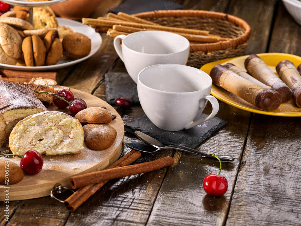 Rolled biscuit and sand chocolate cookies on board. Cinnamon stick and cherry on kitchen wood table in rustic style. Traditional dish. Rolled biscuit and sand chocolate cookies on board. Cinnamon stick and cherry on kitchen wood table in rustic style. Traditional dish.