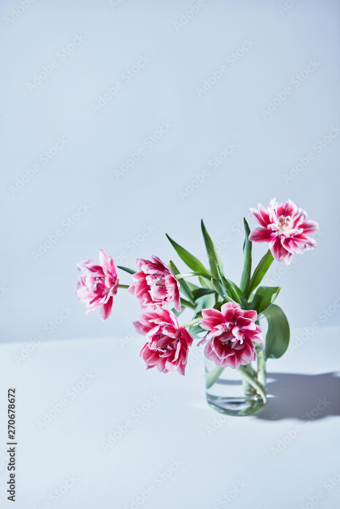 Tulips are pink terry in a bouquet with green leaves in a glass Tulips are pink terry in a bouquet with green leaves in a glass