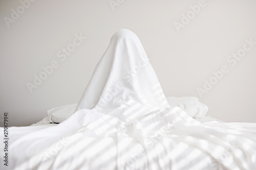Boy hiding under sheet on bed photo