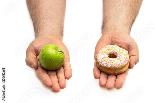 Hands holding an apple and a doughnut concept of a tough choice between opposite alternatives (healthy food vs sweet food)