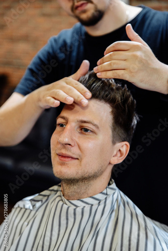Men's haircut and hair styling. Hairdresser does a haircut to a young guy in barbershop