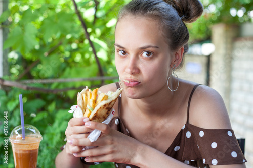 beautiful young girl with pleasure eating a hamburger  Greek gyros   girl in a dress sitting in a street cafe  eating a hamburger