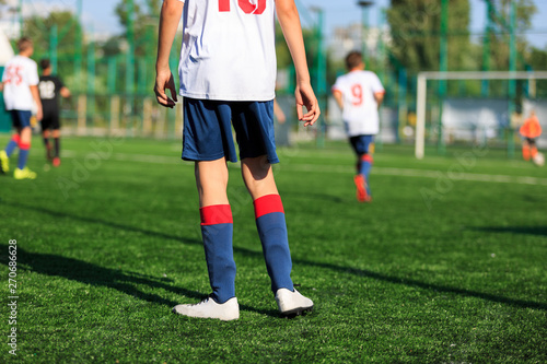 Boys at blue white sportswear run, dribble, attack on football field. Young soccer players with ball on green grass. Training, football, active lifestyle for kids 