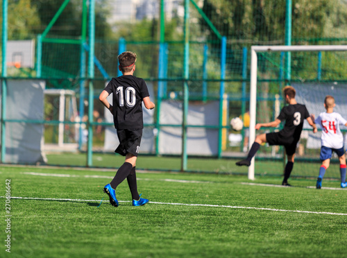 Boys in white and black sportswear plays football on field, dribbles ball. Young soccer players with ball on green grass. Training, football, active lifestyle for kids concept 