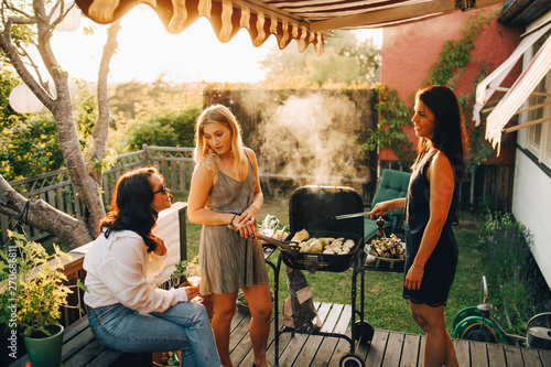 Friends talking while grilling food on barbecue for dinner party in yard photo