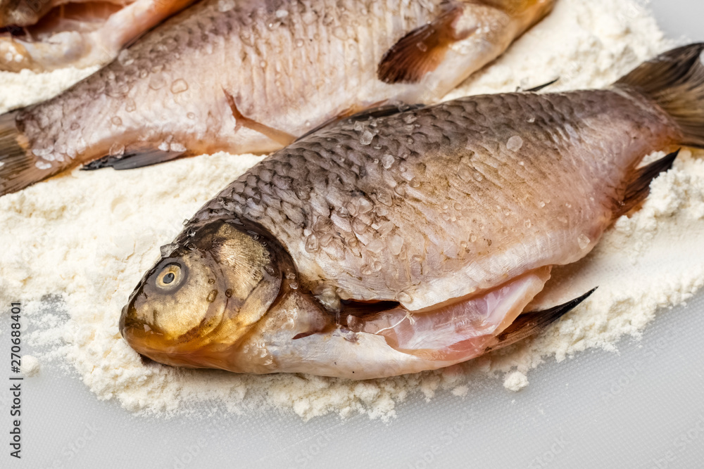 Fresh crucian fish with coarse salt in flour on a white cutting board. Cooking, close up. Copy space Fresh crucian fish with coarse salt in flour on a white cutting board. Cooking, close up. Copy space