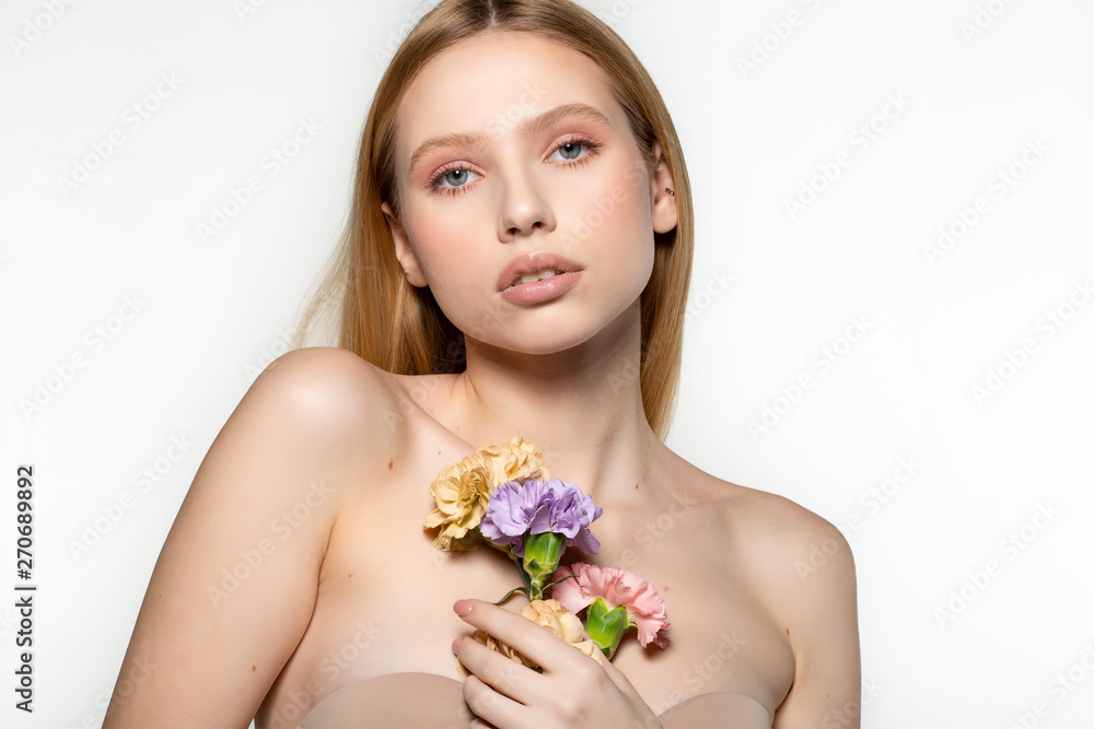 Pretty young blonde girl with trendy makeup and ping flower curled in hair, holding flowers on the shoulder. Studio photo on grey background Pretty young blonde girl with trendy makeup and ping flower curled in hair, holding flowers on the shoulder. Studio photo on grey background