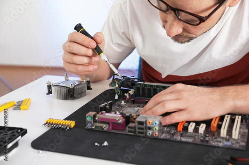 Male technician repairing motherboard at table, closeup