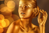Portrait of beautiful lady with gold paint on skin against blurred lights, closeup