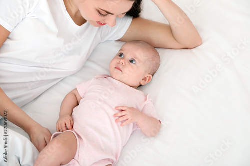 Cute baby with mother lying on bed, above view. Space for text