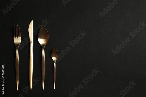 Set of gold cutlery on black background, flat lay. Space for text