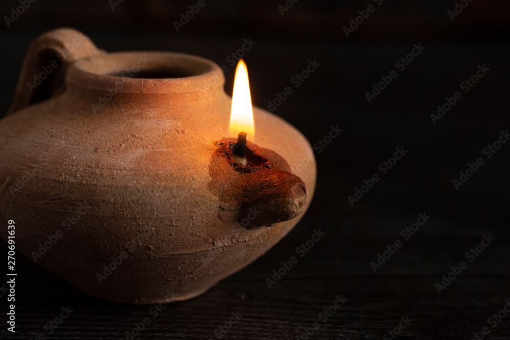 A Lit Handmade Oil Lamp from the Middle East on a Dark Table - obrazy, fototapety, plakaty 