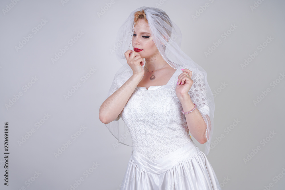 pretty curvy adult woman with short hair wearing long vintage wedding dress with sun style skirt. young caucasian bride with veil on white studio background alone.