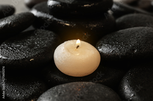 Small burning candle on beautiful wet spa stones